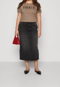 Brun t-shirt med texten "FIERCE", svart denim midi-kjol, röd handväska och svarta ballerinaskor. Har en figursydd silhuett och minimalistisk design.