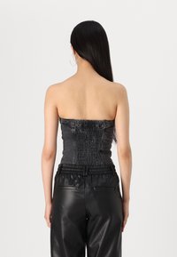 Top nero senza spalline con arricciatura testurizzata, abbinato a pantaloni neri in ecopelle a vita alta. Silhouette liscia e aderente.