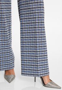 Un pantalon large dans un motif pied-de-poule bleu, noir et blanc, associé à des talons aiguilles argentés avec une finition scintillante.