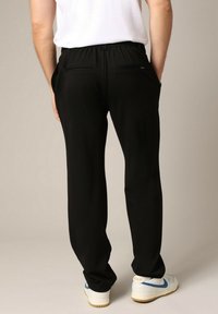 Zwarte, lichte broeken met een trekkoord in de taille, voorzien van twee achterzakken en zijzakken, gedragen met witte sneakers.