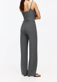 Pantalon gris à jambes larges et taille haute, réalisé dans un tissu texturé. Associé à un débardeur côtelé et ajusté. Design simple, accents minimalistes.