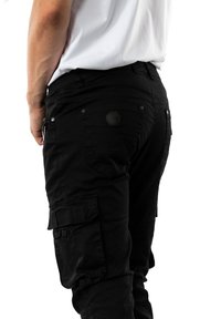 Pantalones cargo negros hechos de un tejido duradero, con múltiples bolsillos, una superficie texturizada y un parche con el logo en la cintura trasera.