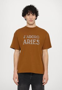 Brown cotton T-shirt with a crew neck and short sleeves, featuring a glittery silver text design reading “J'ADORE ARIES.”