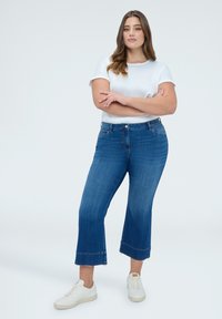 Modré džínové kalhoty do půli lýtek s rozšířeným lemem, vysokým pasem a jemným vyblednutím. Kombinovány s jednoduchým bílým tričkem a bílými teniskami.