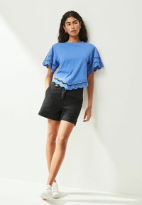 Blauw T-shirt met korte mouwen, versierd met kant en golvende randen, gecombineerd met zwarte shorts en witte sneakers. Gladde stoftextuur.