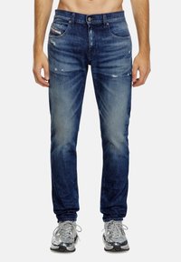 Dark blue denim jeans with a fitted design, featuring a faded front, distressed accents, and five-pocket styling.