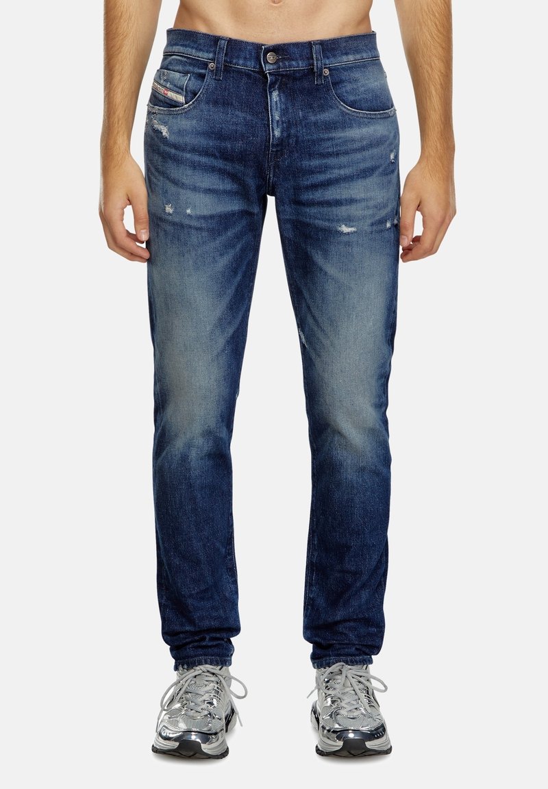 Dark blue denim jeans with a fitted design, featuring a faded front, distressed accents, and five-pocket styling.