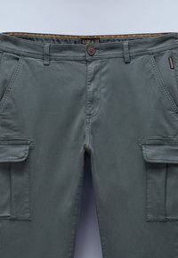 Tummanharmaat cargo-housut, valmistettu puuvillasta, joissa on kaksi sivutaskua, nappisuljenta ja kontrastivärinen sisempi vyötärönauhan kuvio.