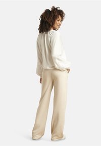 White blouse with intricate embroidered cuffs, paired with cream-colored, wide-leg trousers, presented in a neutral background.