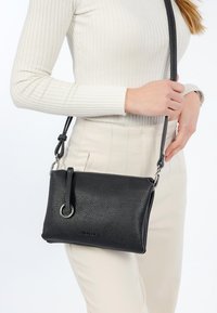 Borsa a tracolla in pelle nera con una finitura testurizzata, dotata di un anello in metallo argentato, manico corto e tracolla regolabile.