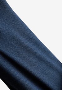 Tissu bleu foncé avec une texture fine et tissée serrée, présenté en angle sur un fond clair.