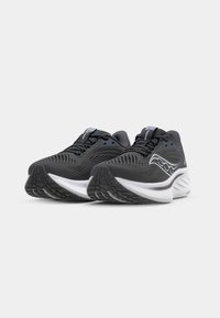 Baskets de sport noires avec des tiges en mesh, semelles intermédiaires blanches et semelles en caoutchouc à motif. Elles comportent des lacets noirs et un logo sur le côté.