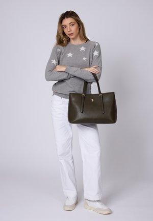Borsa a tracolla in pelle verde oliva con doppi manici e un emblema dorato. Il modello indossa un maglione grigio con motivi a stelle bianche e pantaloni bianchi.