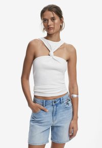 Vit, figurnära ärmlös topp med tvinnat knutdetalj vid halsringningen. Matchas med ljusblå denimshorts med blommönster på fickorna.