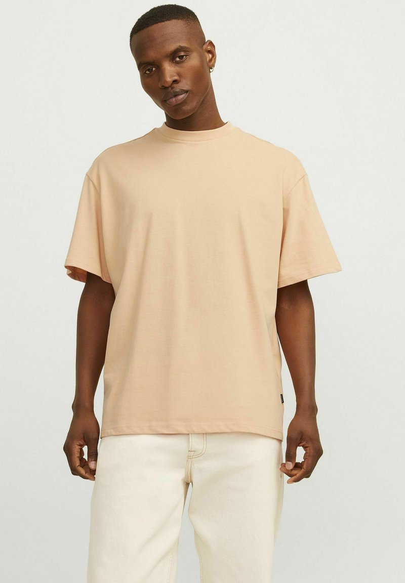 Lys ferskenfarvet oversized T-shirt lavet af blødt bomuld, med korte ærmer og rund halsudskæring, parret med off-white bukser.