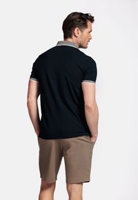 Marineblauwe polo met gestreepte kraag, korte mouwen en beige shorts. De achterkant toont de stoftextuur en pasvorm.