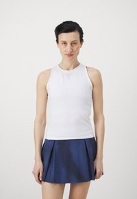 Balts krekls bez piedurknēm ar augstu apkakli, kombinēts ar tumši zilu kroku svārku. Gluda auduma tekstūra ar smalku rakstu un izsmalcinātu griezumu.