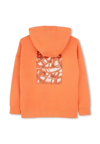 Sweat à capuche orange avec une capuche, présentant une découpe carrée dans le dos qui révèle une couche à motif blanc et marron en dessous. Texture de tissu douce.