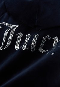 Felpa in velluto blu navy con grande scritta "Juicy" decorata con brillanti di varie dimensioni. Tessuto morbido e trama vellutata.