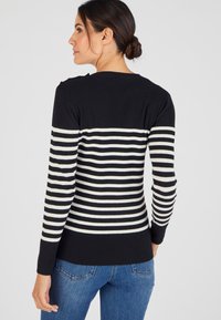 Zwarte geribbelde trui met witte horizontale strepen. Heeft een slim fit ontwerp en lange mouwen, met een ronde halslijn en schouderdetails.
