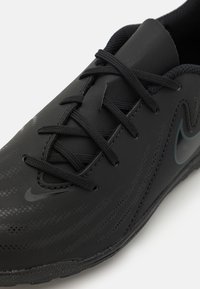 Chaussure de sport noire avec une tige synthétique lisse, un motif texturé, des lacets ronds et un logo subtil dans une teinte plus foncée.
