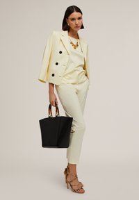 Gelber doppelt-knöpfiger Blazer, passendes Satinoberteil und -hose, schwarze Tote-Tasche mit Schildpattgriffen, beiges Riemchenhochschuh.