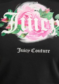 Melna auduma virsma ar lielu rozā rožu un zaļu lapu grafiku, ar baltu tekstu, kas lasāms "Juicy" un "Juicy Couture" izteiksmīgā fontā.