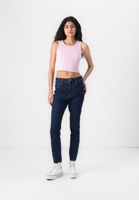 Lõikega roosa lühike tops, tume sinine kõrge vöökohtadega teksapaar, pahkluuni ulatuv, denimiteksituur, koos valgete kõrge säärega tennisetossudega. Lihtne disain.