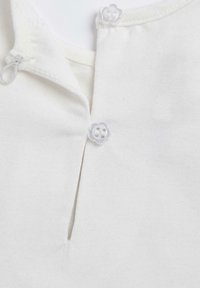 Tela blanca con una abertura estrecha en el escote, asegurada por dos botones transparentes en forma de flor, con una textura textil suave.