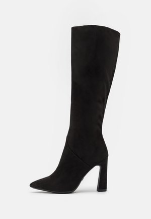 Schwarze kniehohe Stilettostiefel aus weichem Wildleder, mit einer spitzen Zehenform und einem klobigen Absatz, in einem schlanken, nahtlosen Design und matter Oberfläche.