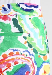 Barevná sukně s květinovým vzorem, která má zelené pozadí s víry modré, růžové, oranžové a bílé barvy, s detailem zadní kapsy.