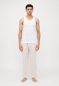 Camiseta sin mangas blanca de algodón combinada con pantalones de lino gris claro. La camiseta tiene un cuello redondo y los pantalones son holgados y de largo completo.