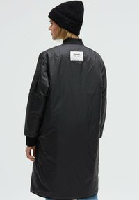 Black padded jacket with a ribbed collar and cuffs. Showcases a large back label and a sleek, shiny texture. Features side pockets.