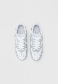 Para białych i jasnoszarych sneakersów Nike Air Force 1 z białymi sznurówkami, widziana z góry na jednolitym białym tle.