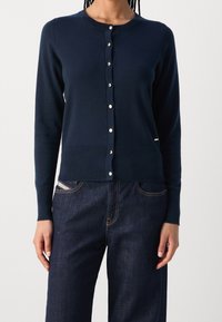 Navy modrý pletený kardigan s kulatým výstřihem, dlouhými rukávy a knoflíkovým zapínáním s malými, lesklými akcenty. Texturovaná látka.