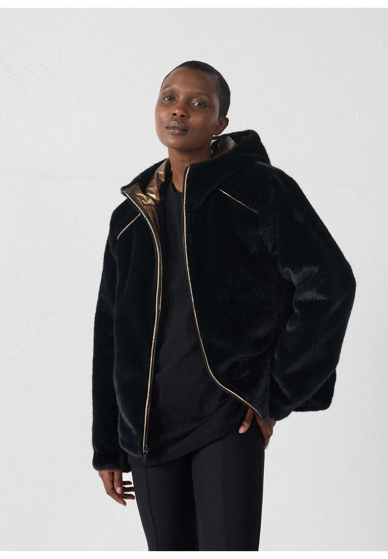 Chaqueta negra de pelaje sintético con capucha, zipper dorado y forro interior. Presenta un corte relajado y una textura suave.