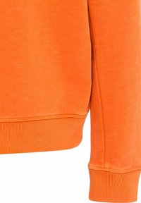 Manche et ourlet inférieur de sweat-shirt orange avec poignets côtelés sur un fond uni.