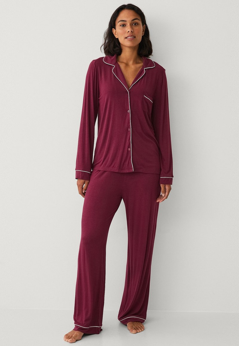 Bordó pyžamo z měkké látky. Halenka s dlouhým rukávem a knoflíky, s bílým lemem a jednou náprsní kapsou. Odpovídající volné kalhoty.