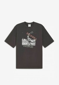 T-shirt in cotone grigio scuro con maniche corte, caratterizzato da una stampa grafica di una figura e dal testo "Diadora Palmes" in colori a contrasto.