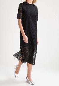 Svart spetsklänning med korta ärmar, rund halsringning och sidoklyvning. Matchad med silverfärgade blockklackskor. Strukturerad spetsmönster.