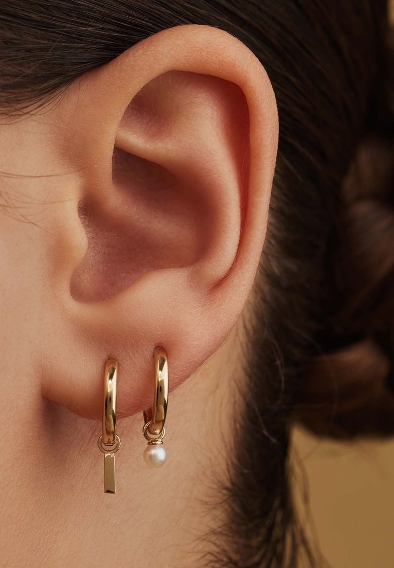 Goldene Creolen mit einem kleinen rechteckigen Anhänger und einer weißen Perle, die ein poliertes Finish und ein schlichtes, elegantes Design zeigen.