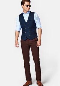 Navy dwurzędowa kamizelka na jasnoniebieskiej koszuli, w połączeniu z brązowymi spodniami slim-fit i brązowymi skórzanymi butami. Charakteryzuje się eleganckim designem i dopasowaniem.