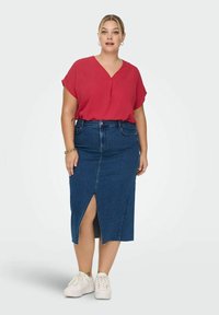 Röd kortärmad blus med V-ringning, tillsammans med en mörk denim blyertskjol med en främre slits, bärs med vita sneakers.