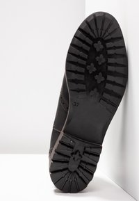 Černá podrážka boty s texturovaným gumovým povrchem se vzorem běhounu ve tvaru hvězdy a označením velikosti 37. Navržena pro odolnost a přilnavost.