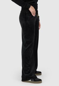 Melni velūra sporta bikses ar taisnu piegriezumu, kurām ir sānu kabatas un elastīga josta. Audumam ir gluda tekstūra ar maigu spīdumu.