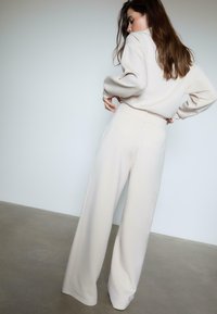 Bredde beige bukser med en glat tekstur og minimalistisk design, der har to baglommer og en høj talje, parret med en matchende top.