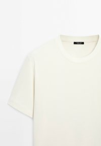 En enfärgad off-white t-shirt med kort ärm och rund halsringning, med en svart etikett inuti kragen.