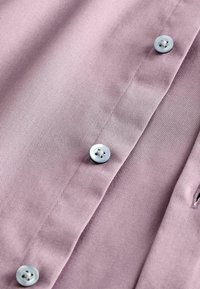 Camicia viola chiaro caratterizzata da una texture di tessuto liscia, con chiusure a bottone e un motivo a ribes diagonale. I dettagli includono bottoni blu chiaro.