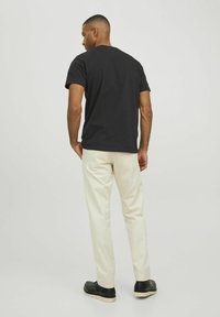 T-shirt nera in cotone a maniche corte, abbinata a pantaloni in cotone color crema. Il tessuto crema è liscio; le scarpe sono nere con suole di colore chiaro.