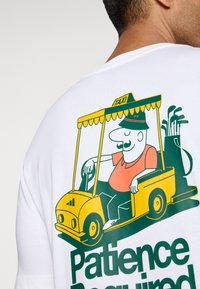 White t-shirt with a graphic of a yellow taxi cart and a cartoon driver. Text reads "Patience Required" in green below the graphic.